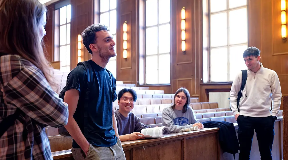 Vier Studierende stehen in einem Hörsaal zusammen und unterhalten sich