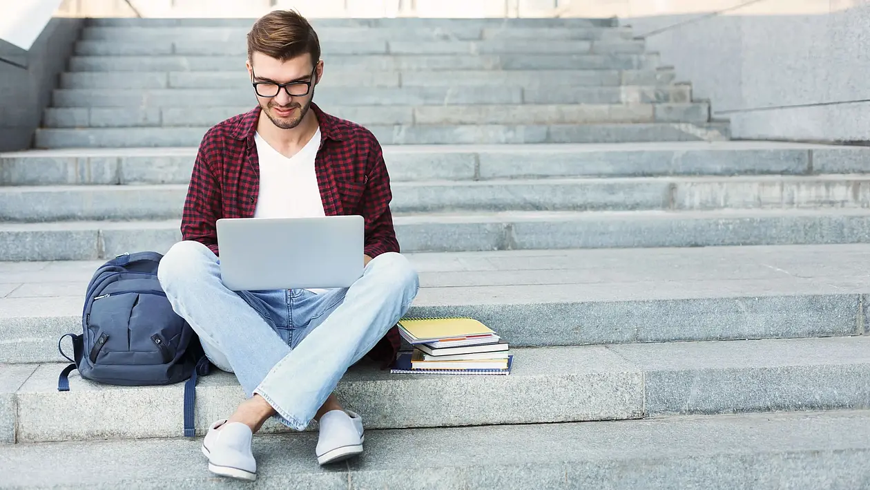 Foto einer Person, welche mit einem Laptop auf einer Treppe sitzt und damit arbeitet.