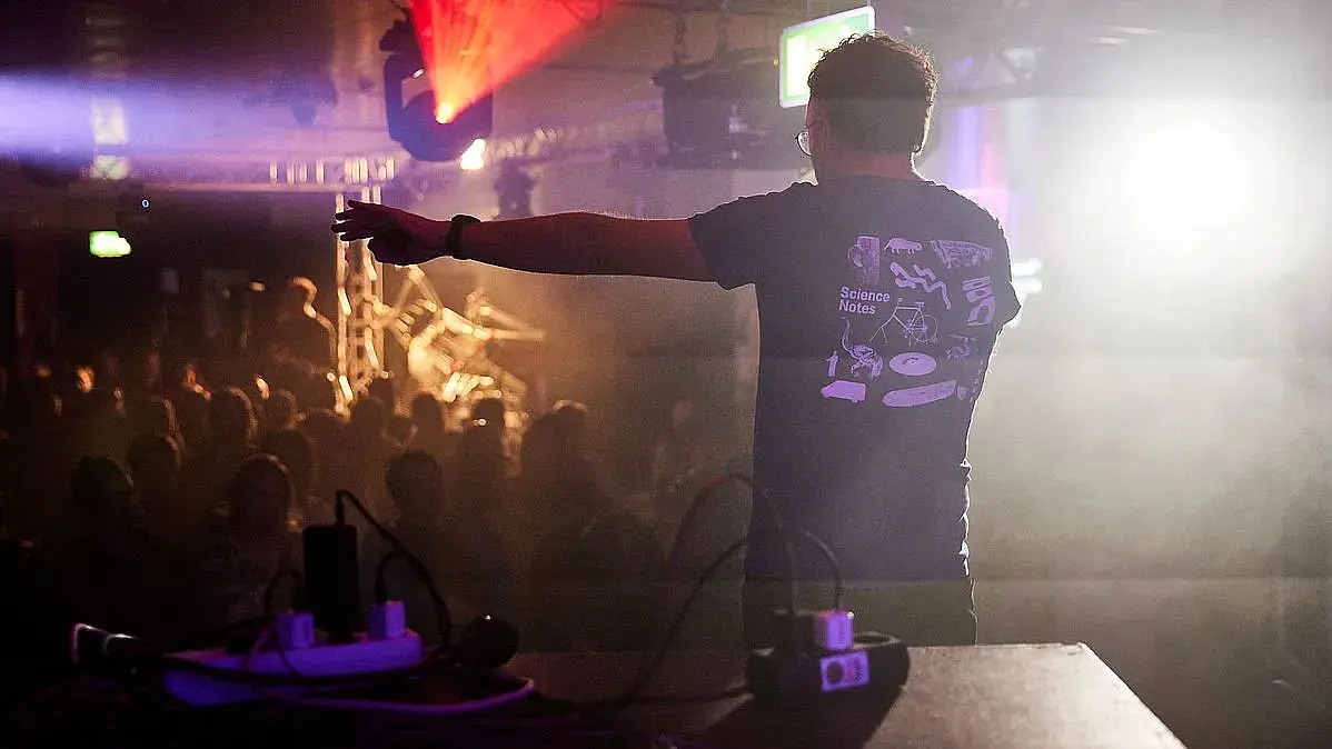 Im Mann in einem Tanzclub steht im Gegenscheinwerferlicht und spricht ins Publikum. Science Notes