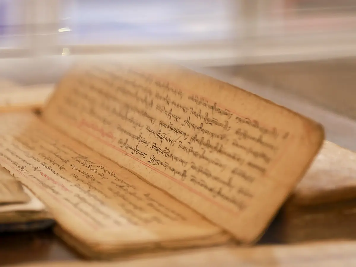 Auf dem Bild liegt ein vergilbtes Papier auf einem Tisch. Auf dem Papier drängen sich die Wörter eng aneinander und die Schrift ist sehr klein.