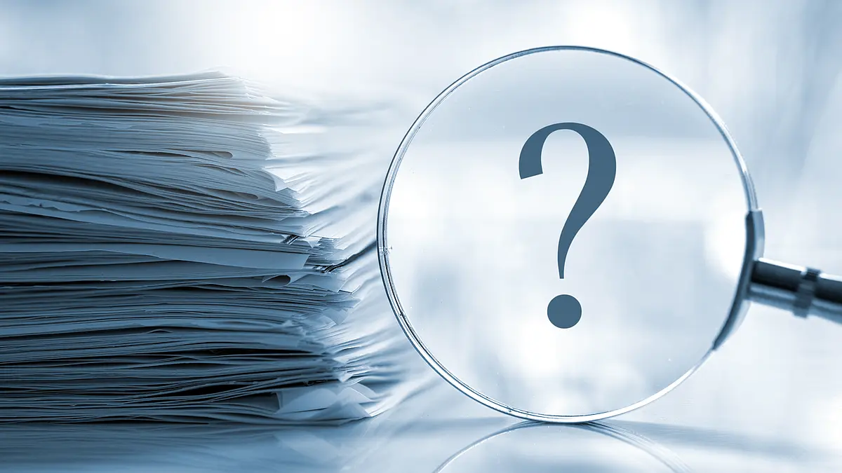 pile of documents, in front of it a lens with an enlarged question mark