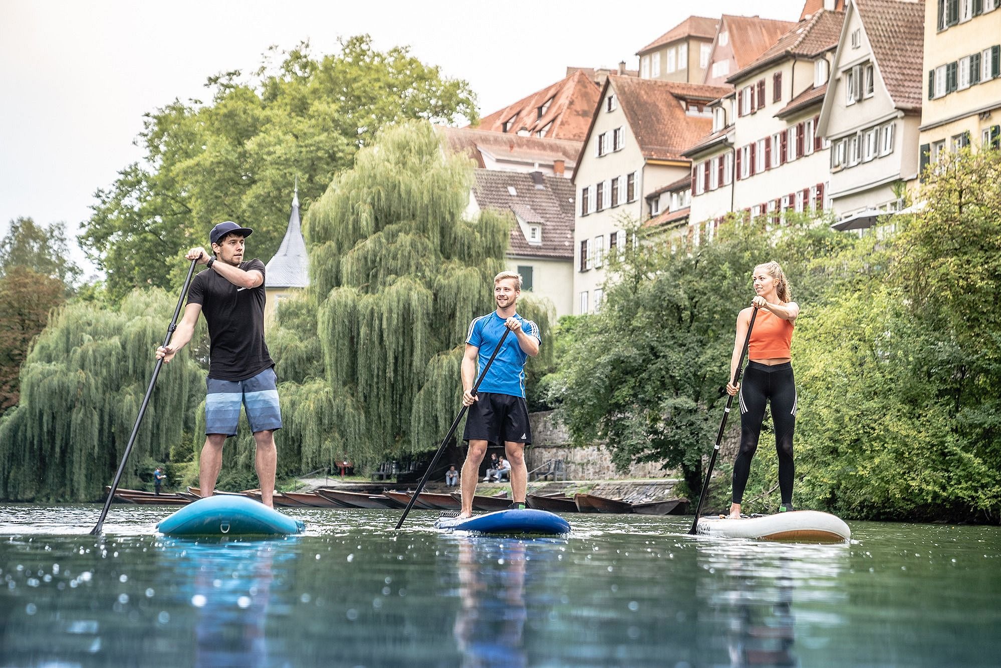 Three persons each on a SUP on the river Neckar in front of timbered houses