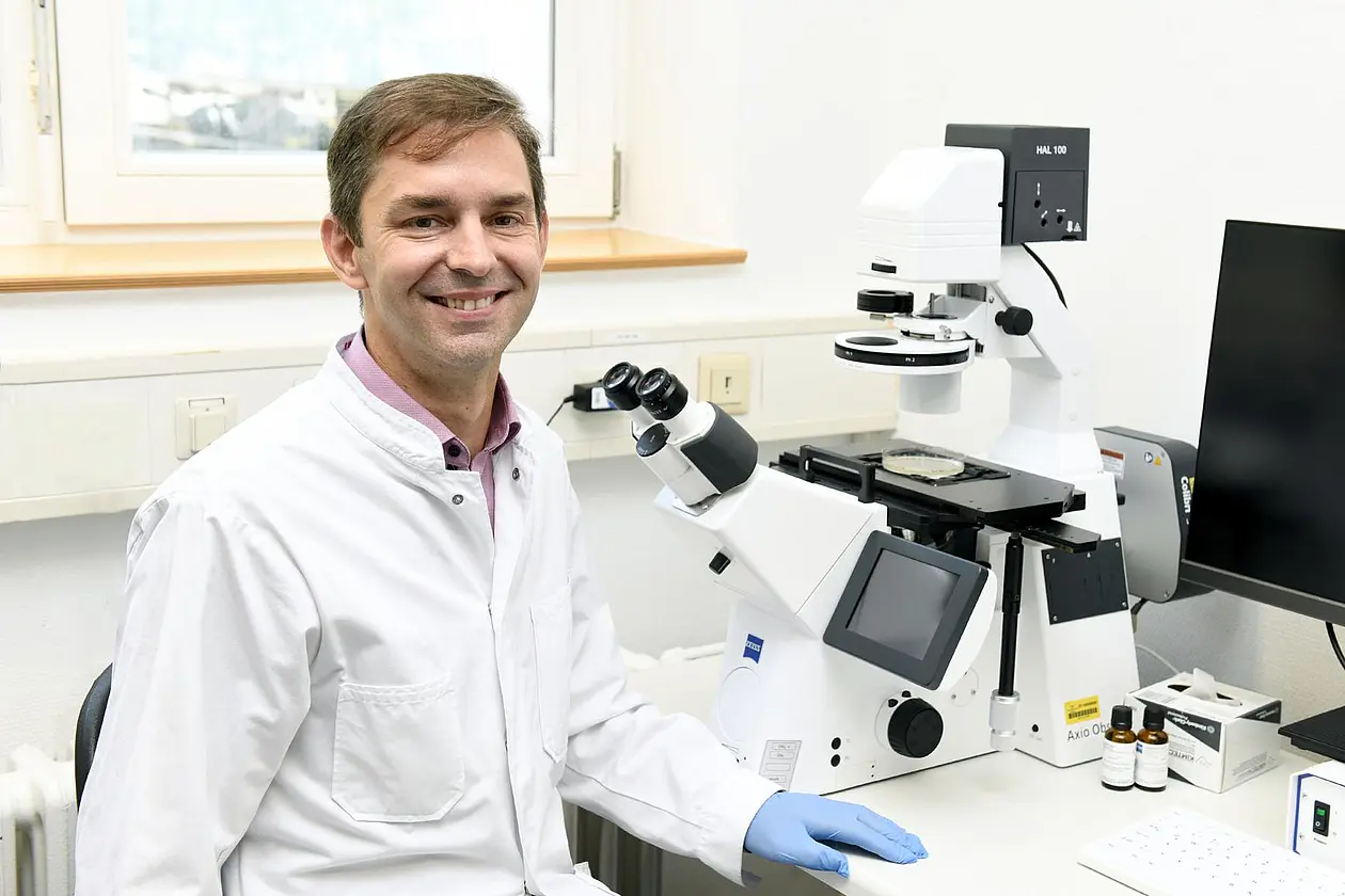 Researcher in lab coat and rubber gloves in front of microscope