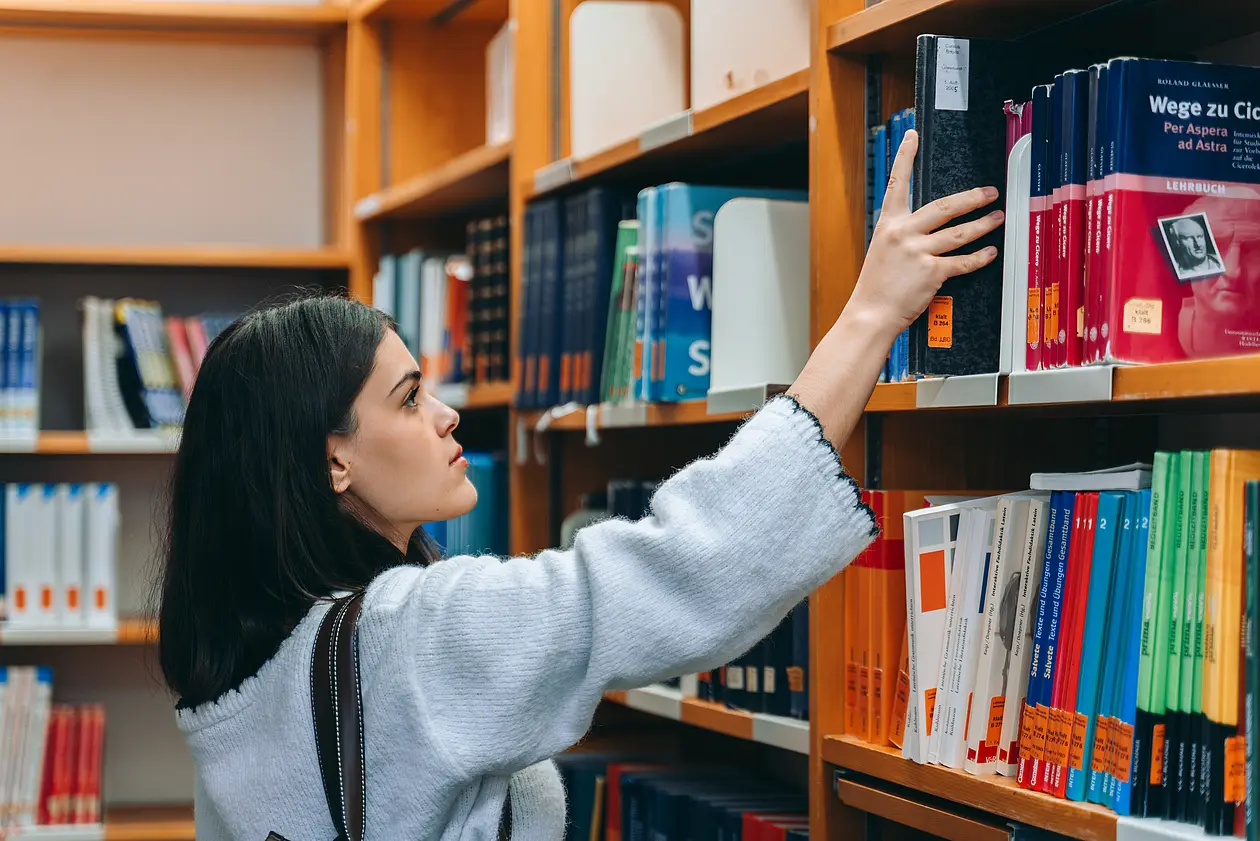 Eine Studentin nimmt ein Buch aus einem Regal in der Universitätsbibliothek.