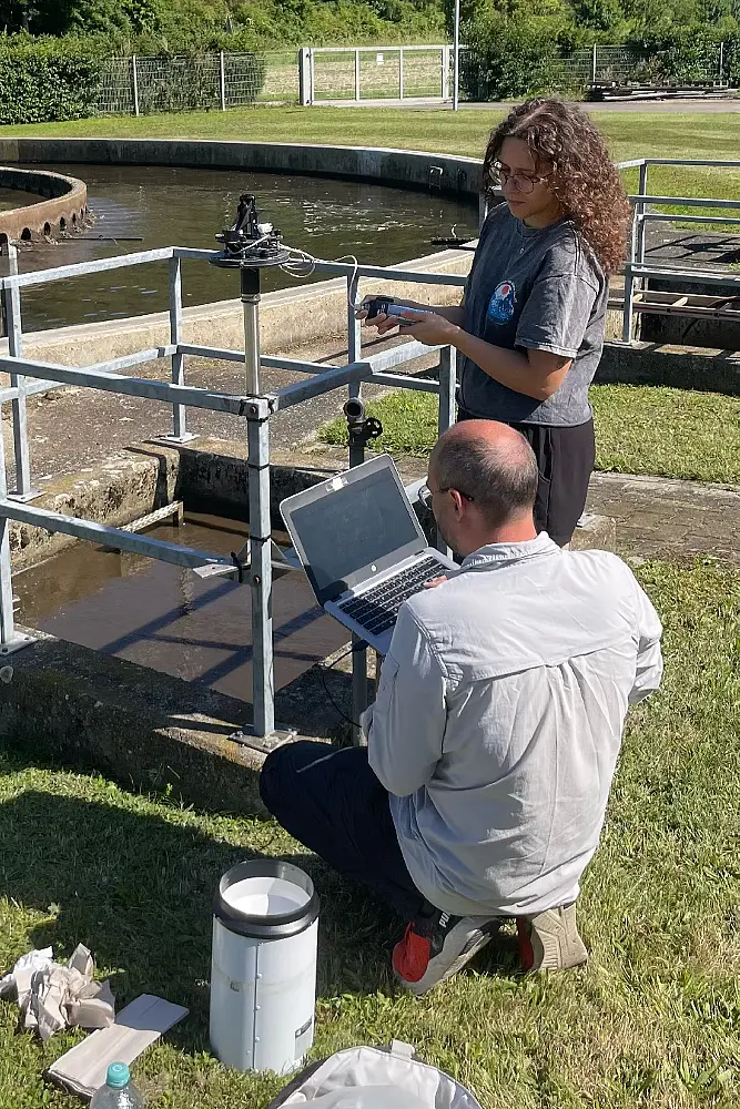 Zwei Personen im Feld lesen Dateien aus einem Regenwassersammler aus auf einen Laptop.