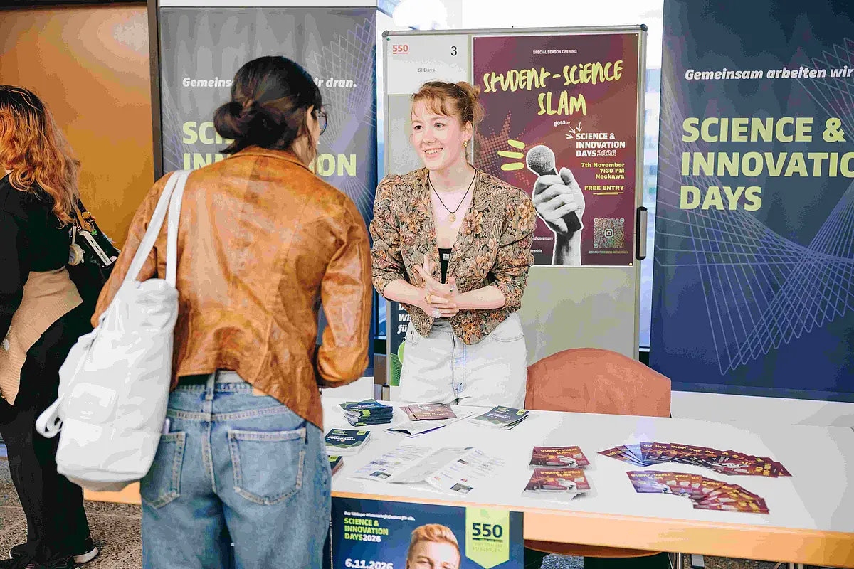 Zwei Frauen unterhalten sich an einem Stand. Im Hintergrund sind Plakate der Science& Innovation Days.