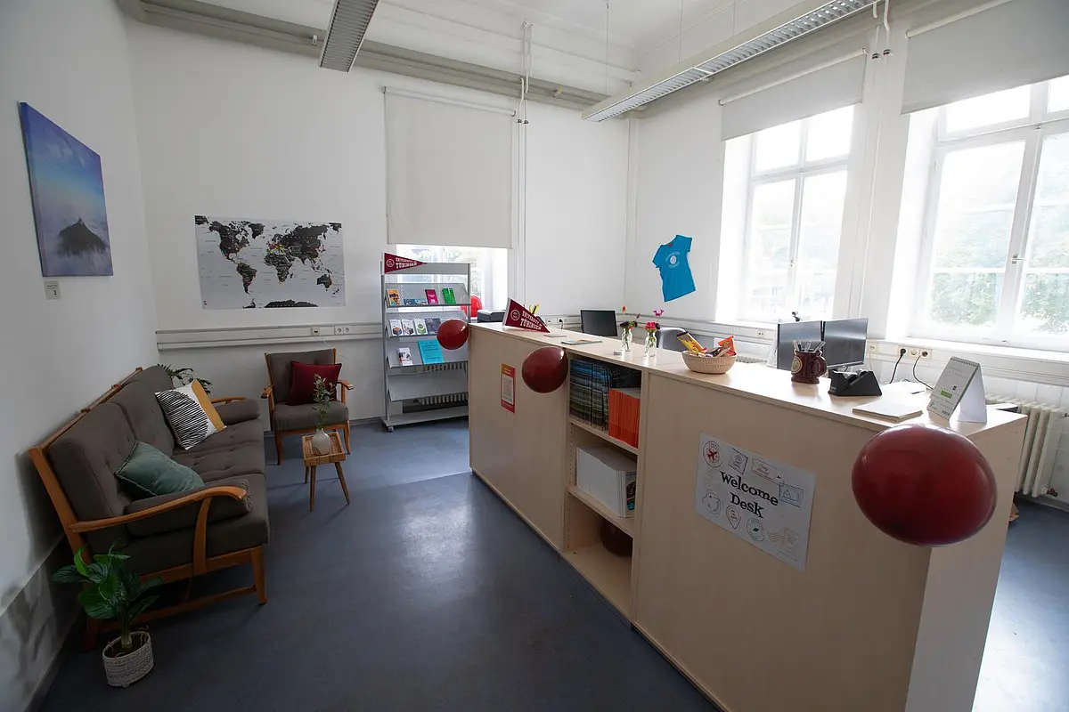 Foto der Theke des Welcome Desk, dahinter Schreibtische, links davor ein Sofa