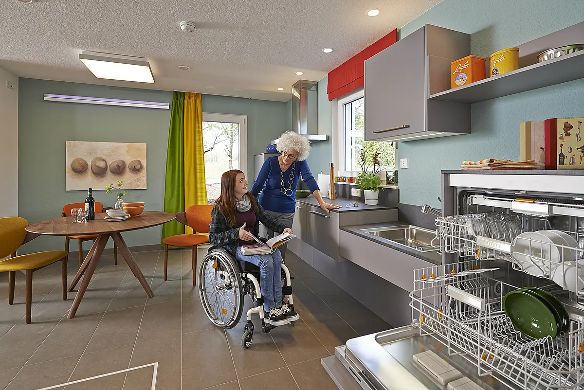 A woman in a wheelchair and another woman in the kitchen.