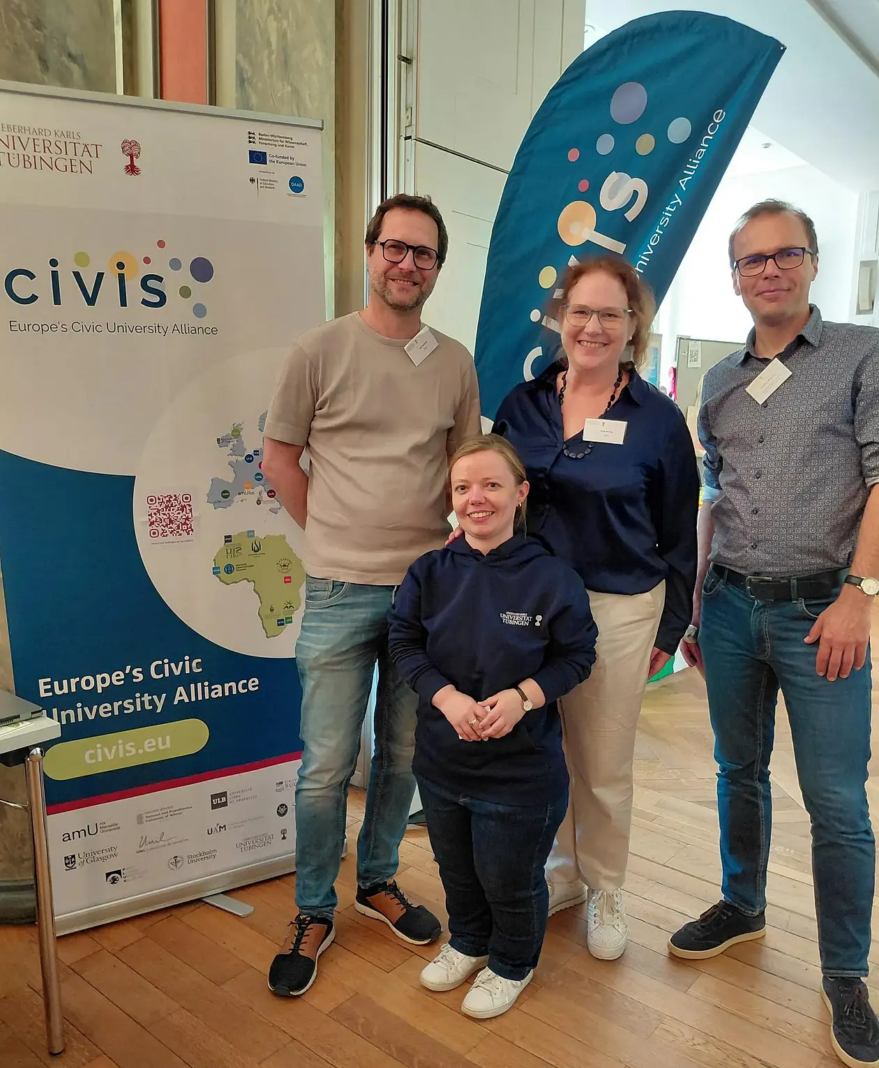 Vier Team-Mitglieder stehen vor Roll-up und Fahne mit CIVIS-Logo