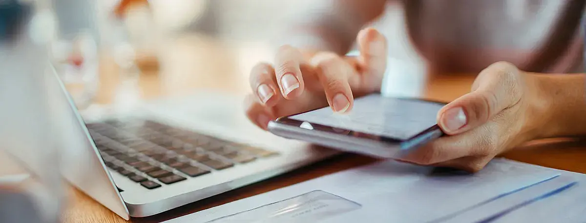 Eine Person hat ein Handy in der Hand und hat auch ein Laptop vor sich.