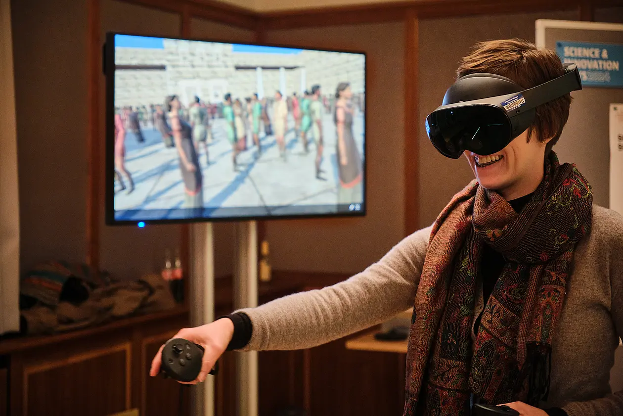 Eine Frau mit VR-Brille, hinter ihr ein Monitor.