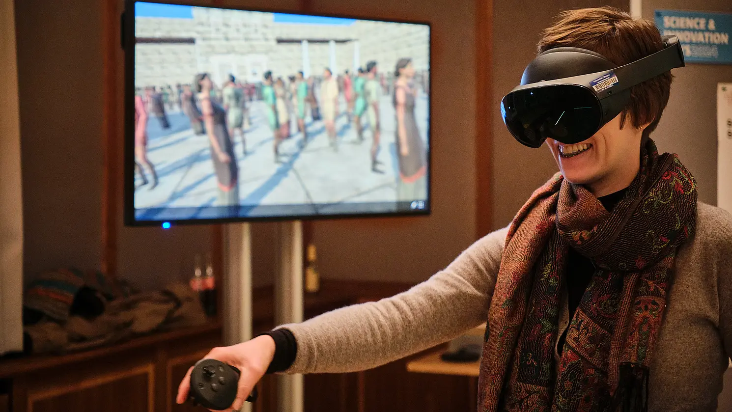 Eine Frau mit VR-Brille, hinter ihr ein Monitor.