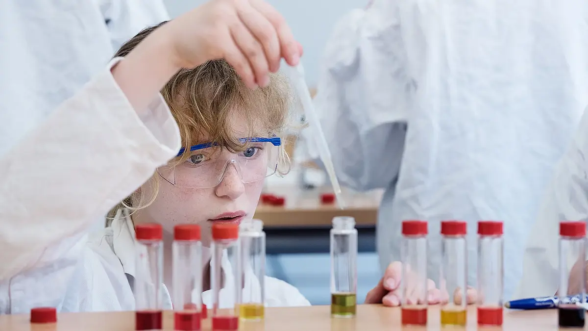 Das Bild zeigt ein Kind, das Reagenzgläser mit einer Pipette befüllt.