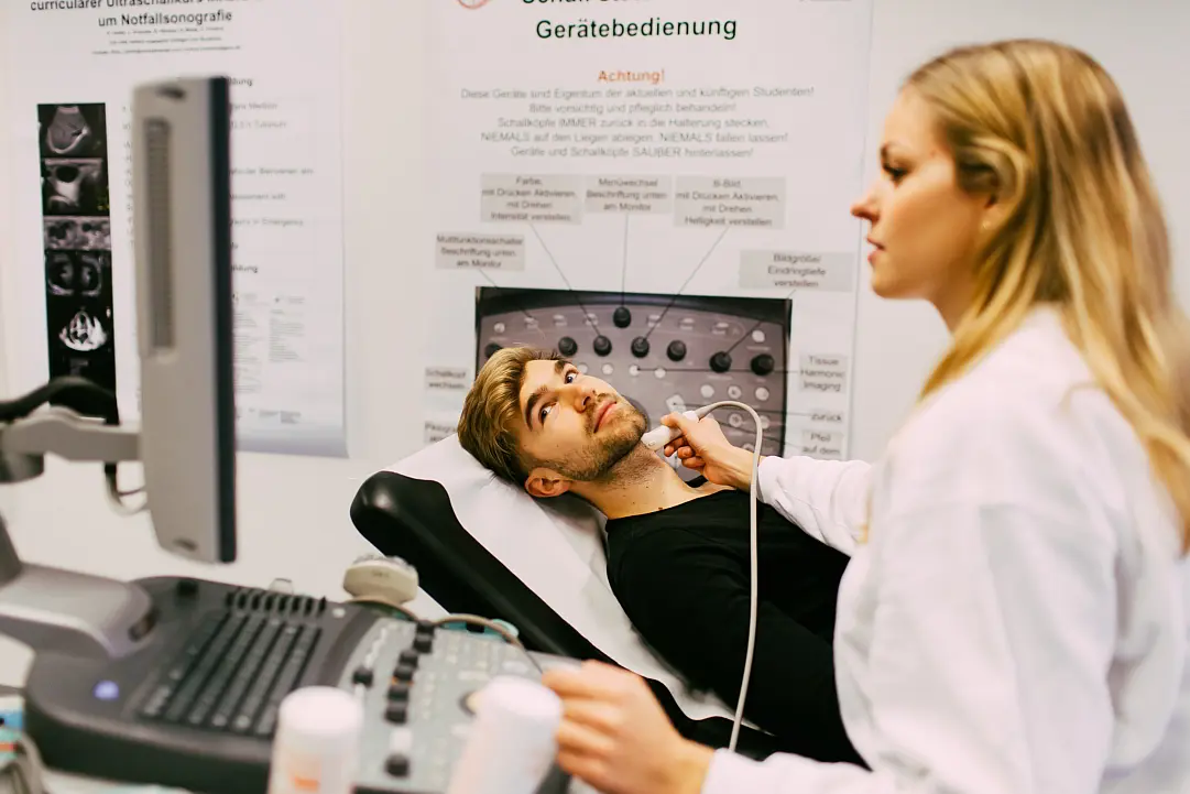 Eine junge Medizinstudentin untersucht einen jungen Mann mit einem Ultraschallgerät am Hals