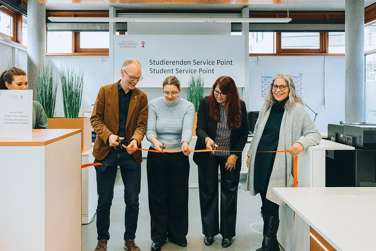 Vier Personen halten ein orangenes Band, drei von ihnen sind dabei, das Band durchzuschneiden. Im Hintergrund an der Wand der Schriftzug "Studierenden Service Point"