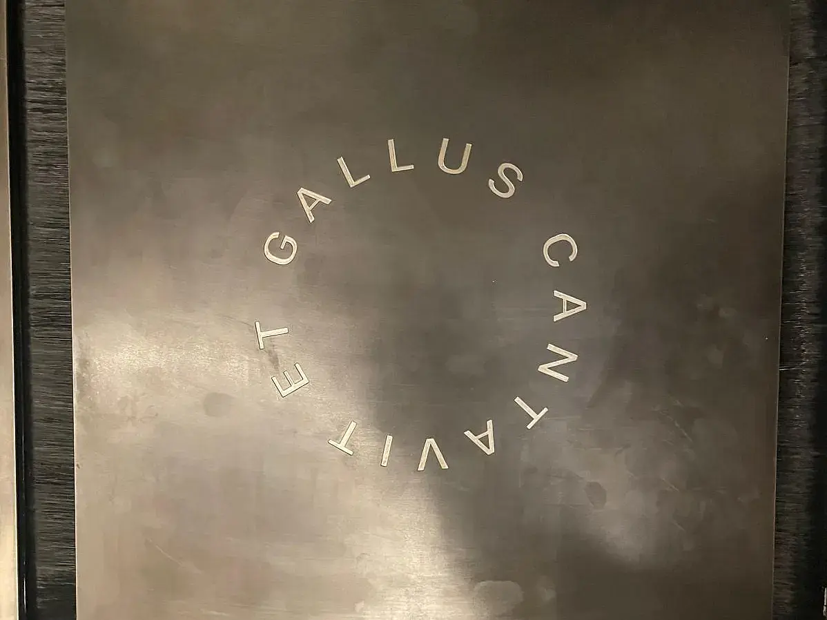 Zu sehen ist ein Schriftzug in Kreisform. Der Schriftzug lautet: Et Gallus cantavit" ca