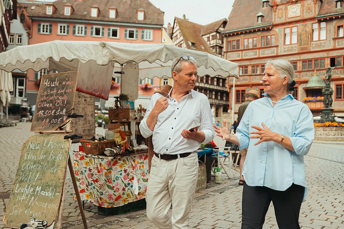 Rektorin im Gespräch auf dem Marktplatz, im Hintergrund ein Marktstand und das Rathaus