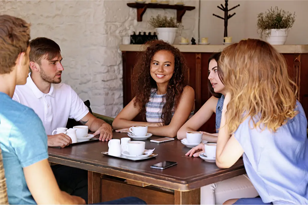 Five students having a conversation while sitting around a table in a cafe.