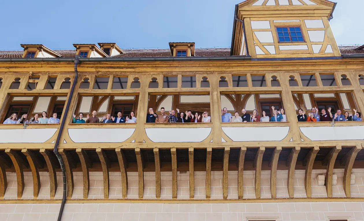 Die Teilnehmenden des HCoN Treffens winken vom Balkon des Schlosses in Richtung des Schlosshofes. Der Fotograf hat vom Hof aus fotografiert. 