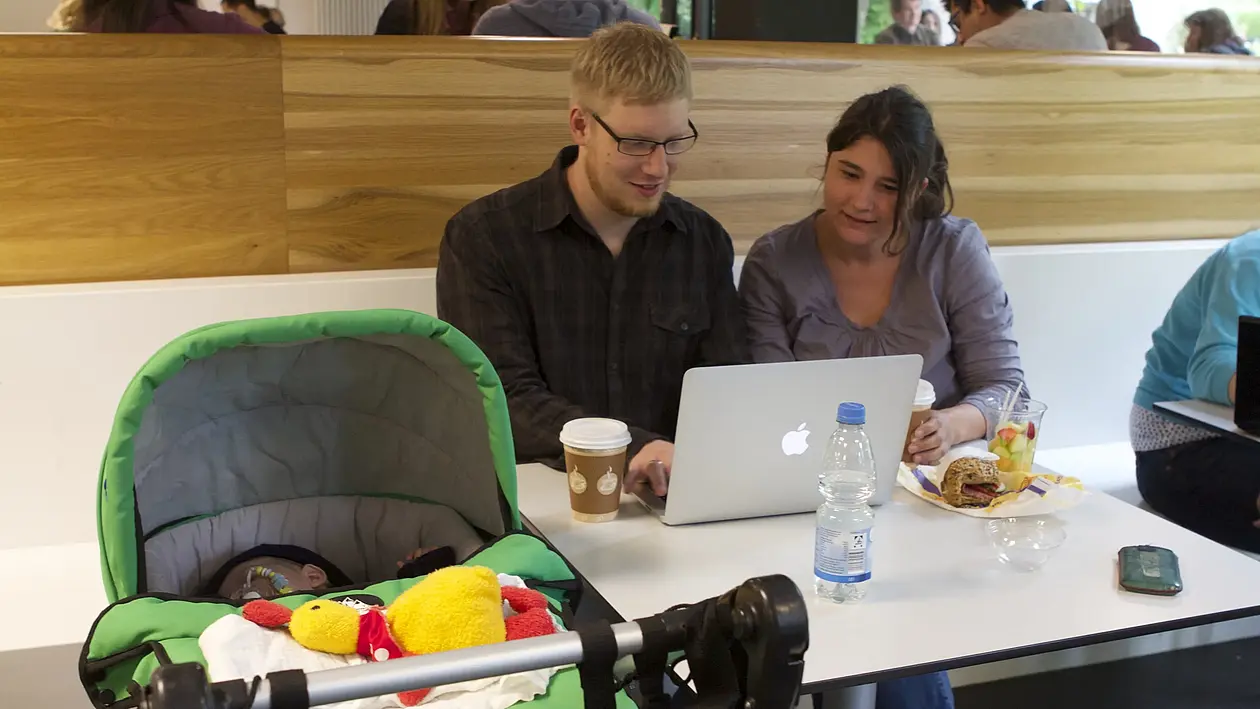 Tile icon showing a young couple with a pram in front of a laptop in a public space (linked to the "Working with children“)