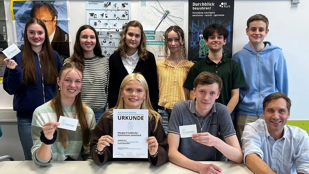 Neun Schülerinnen und Schüler in zwei Reihen hintereinander mit ihrem Lehrer. In der Mitte zeigt eine Schülerin die Urkunde.