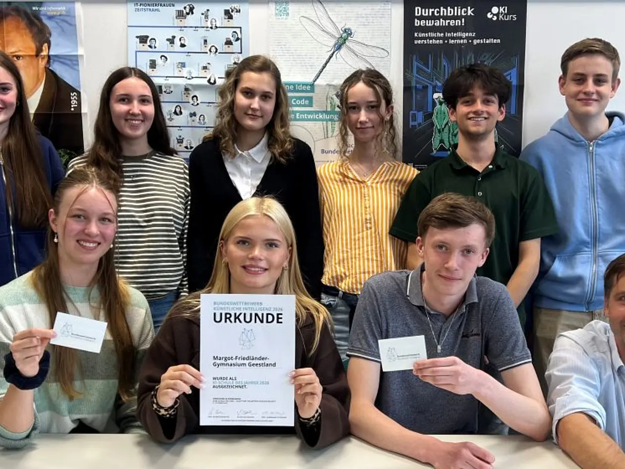 Neun Schülerinnen und Schüler in zwei Reihen hintereinander mit ihrem Lehrer. In der Mitte zeigt eine Schülerin die Urkunde.