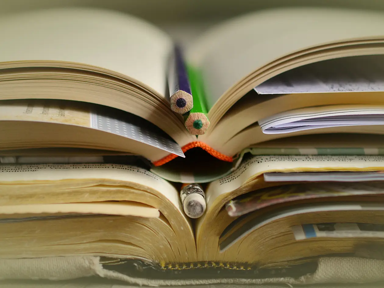 Aufgeschlagene Bücher liegen aufeinander mit Lesezeichen und Stiften