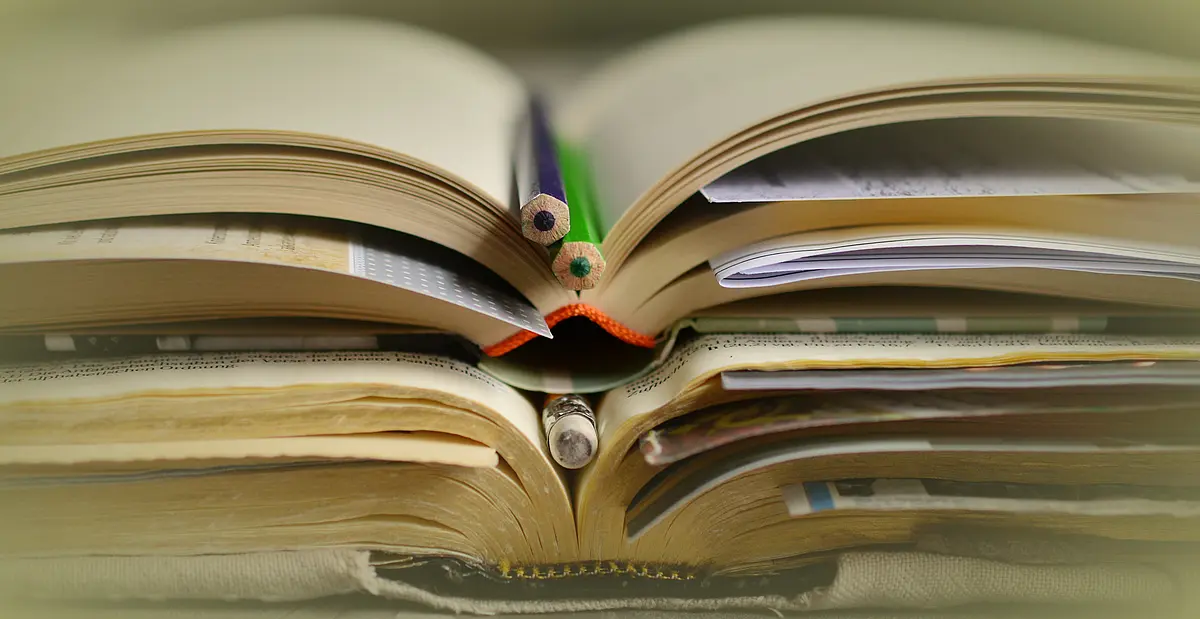 Aufgeschlagene Bücher liegen aufeinander mit Lesezeichen und Stiften